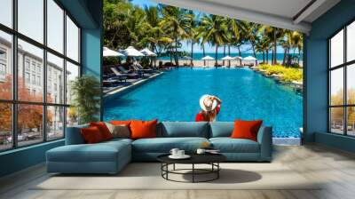 Luxury beach vacation in tropical beach hotel. Tourist woman in red dress relax near blue swimming pool in modern resort. Female traveler on sea vacation. Wall mural