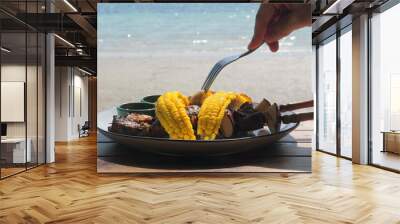 Person eating grilled corn and skewers by seaside, capturing casual meal with ocean view. Summer Vacation and Outdoor Dining. Wall mural