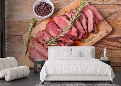 Slices of medium rare roast beef meat on wooden cutting board, pepper and rosemary branches on wooden background. Top view. Gourmet food. Raw meat beef steak. Wall mural