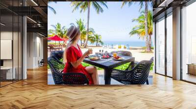 Woman on tropical healthy breakfast in hotel with sandy sea beach, palm trees and swing on background. Salad, fruits and fresh orange juice on morning food. Luxury resort, holidays in Thailand Wall mural