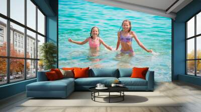 Happy children splashing in the waves during summer vacation on tropical beach. Girls play at the sea. Wall mural