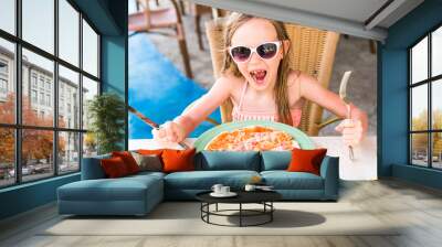 Portrait of cute little girl sitting by dinner table and eating pizza Wall mural