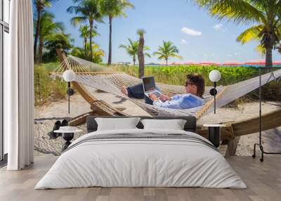 young man working on laptop in hammock at tropical beach Wall mural