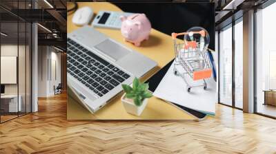 A man sitting at a desk calculates monthly bill expenses online, uses a laptop, makes financial analysis on an account with a pink piggy bank. Saving ideas for the future of investment
 Wall mural