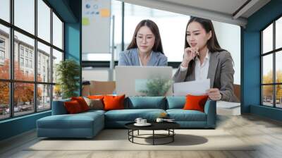 Two women are sitting at a table with a laptop and a stack of papers Wall mural