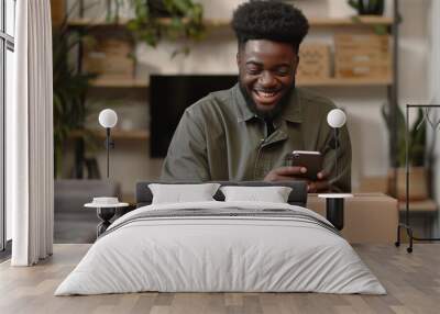 Happy African American client typing on mobile phone over logistic cardboard box, receiving parcel from delivery transportation service, using smartphone, smiling, laughing Wall mural