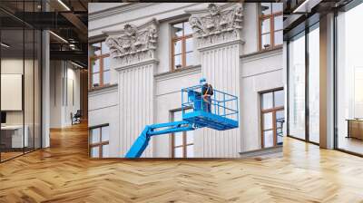 construction worker in lift bucket of crane restore and repair historic facade of building. man in c Wall mural