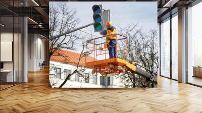 Man in uniform on aerial platform fix and repair broken traffic signal. Traffic lights repair works, worker in lift bucket working at height. Maintenance of public lighting and urban traffic signals Wall mural