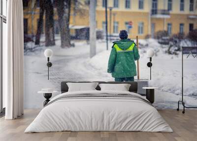 Worker with snow shovel sweep and remove snow, snow removal city service. Janitor in uniform with snowshovel in hands ready to clean snowy sidewalk and walkway during blizzard. Wall mural