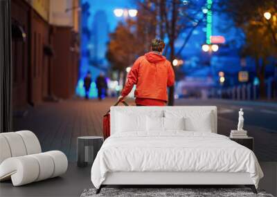 Young deliveryboy walking with red thermal bag on night city street. Man of delivery service in hurry to deliver an order. Delivery service goes to give the order quickly to the client at night Wall mural