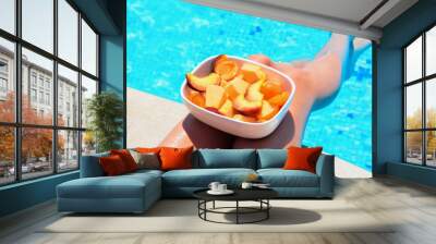 Tanned beautiful legs. Young woman relaxing and eating fruits. Fruits in a bowl by the pool near a thin slender fit girl legs. Fruit salad, healthy food. Summer concept Wall mural