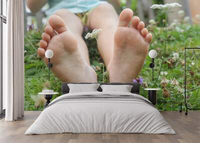 Child feet on green grass, barefoot little girl on meadow, countryside lifestyle, concept of grounding and connecting with nature Wall mural