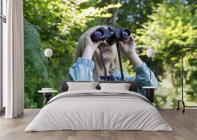 Cute little girl exploring nature looking through binoculars. Child playing outdoors. Kids travel, adventure and bird watching concept. Wall mural