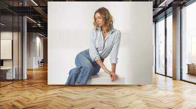 Fashion portrait of young woman in light blue cotton button down shirt and blue jeans on the white background Wall mural