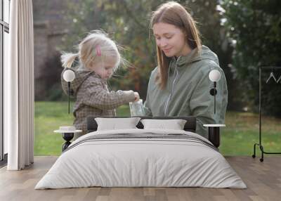 Mother and her toddler girl putting seeds for birds in a bird feeder. Quality outdoor family time together. Encouraging wildlife in the garden with bird feeder. Wall mural