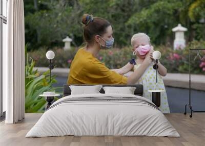 Mummy struggles to put medical mask on her child's face. Reckless toddler girl refuses to wear protective face mask. Parenting challenges during pandemic Corona virus outbreak time. Wall mural