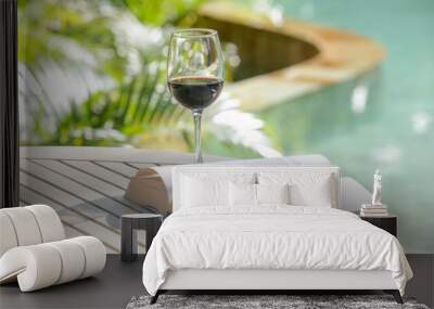 Open book and a glass of red wine on the table next to the swimming pool. Summer day leisure concept. Wall mural