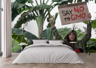 Save NO to GMO. Caucasian woman holding a cardboard sign against genetically modified organisms and genetic engineering in food production. Peaceful environmental activist protest concept. Wall mural