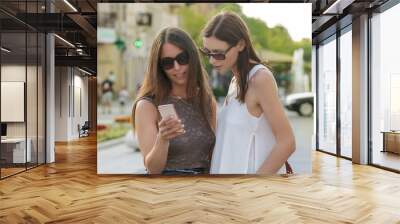 Two friends looking at the mobile phone, two girls hanging out in the city Wall mural