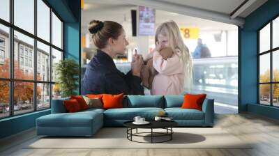 Young woman comforting child lost at the airport who can't find her parents. Mother consoling upset little crying girl which got scared from flight at the airport. Wall mural