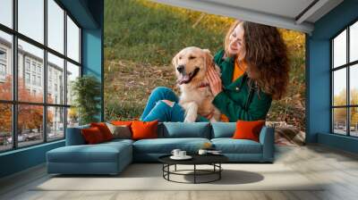 Smiling woman hugging her pet golden retriever dog near face. Golden retriever dog playing with a curly woman walking outdoors sunny day. love and care for the pet. Wall mural