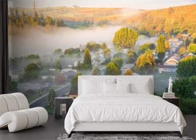 Misty spring landscape with foggy and first ray of early morning light. Aerial view of small valley town at rural of Colfax, Eastern Washington, US surrounded by morning fog, pine trees and empty road Wall mural