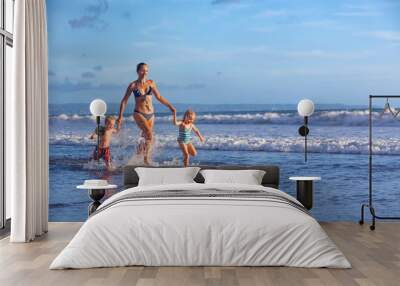 Happy barefoot family having fun - mother, baby son, daughter together run with splashes by water pool along surf of sunset sea beach. Active parent and people activity on summer holiday with children Wall mural