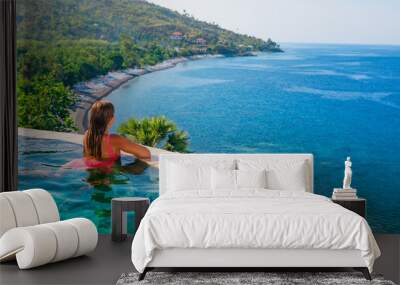 Happy girl have fun on summer beach holiday. Young woman relaxing at edge of infinity swimming pool with sea view from hill top. Healthy family lifestyle, summer travel with kids on tropical islands. Wall mural