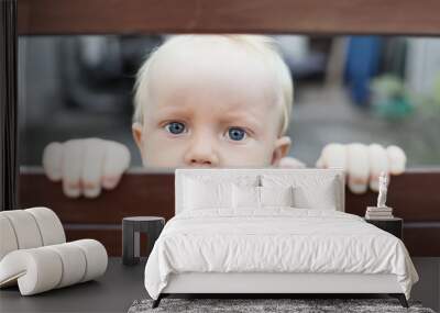 Portrait of abandoned by parents baby boy with staring blue eyes, sad and lonely face expression, looking out through fence. Social problems, family abuse, children stress and negative emotions Wall mural