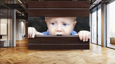 Portrait of abandoned by parents little baby boy with staring blue eyes, sad and lonely face expression, looking out through the fence. Social family problems and children stress and negative emotions Wall mural