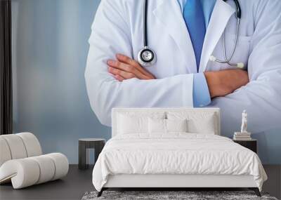 A doctor is wearing a white coat and a blue tie. He is standing with his arms crossed Wall mural