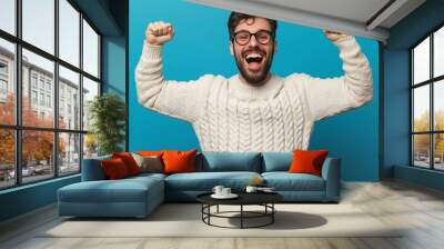 A man in a white sweater is smiling and raising his arms in the air. Concept of joy and excitement Wall mural