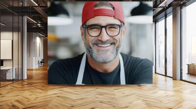 A man with glasses and a red hat is smiling. He is wearing a black shirt and a white apron Wall mural