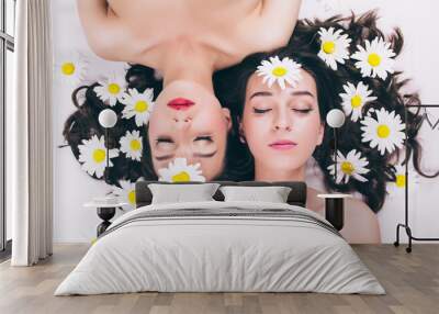 Two trendy topless twin sisters cheerful summer hipster teenage girls in a spa salon lie naked face to face on their backs covered in chamomile flowers. The concept of skin care, health and motherhood Wall mural