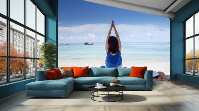 Beautiful asian woman in blue dress practicing yoga on the beach, relaxing with hat and book Wall mural