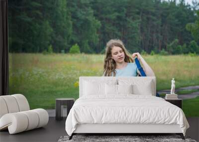 In summer, a teenager girl travels. She is walking along the road with a backpack on her shoulders. Wall mural