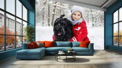 In winter, snow falls in the snowy forest, two little girl play with a big black dog. Wall mural