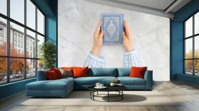 Female hands holding the Quran. Book with Arabic title All Quran. Muslim religious scripture. Marble background. Wall mural