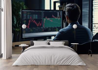 Back view of young businessman sitting at desk in office and looking at computer screen with stock market chart Wall mural