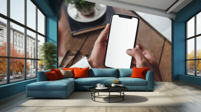 Cropped shot of businessman using smartphone with blank screen while sitting at modern office desk Wall mural