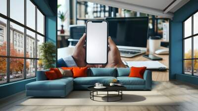 Mockup of a man's hands holding smart phone with blank white screen while sitting at the wooden table in modern office Wall mural