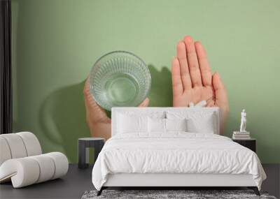 A glass of water is held in the left hand and several white pills placed on the right hand. Medication and prescription pills concept Wall mural