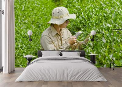 An asian man with a hat on his head is carrying a notebook and a pen, another hand is holding a green tea leaf. Agricultural industry concept Wall mural