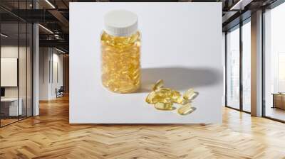 White minimal background features an unbranded clear bottle full filled with yellow multivitamin capsules, which brings countless health benefits. Photo from high angle shot, advertising space Wall mural