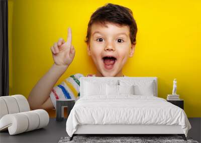 idea. child, boy emotionally points up. A gesture of an idea. Portrait of a child in a bright striped T-shirt on a yellow background Wall mural