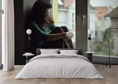 Sad young woman sitting on the window, watching out Wall mural