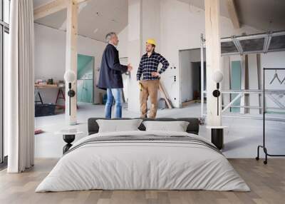 Architect and construction worker discussing while standing in renovating house Wall mural