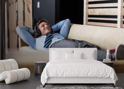 Businessman with headphones lying on couch in office lounge Wall mural