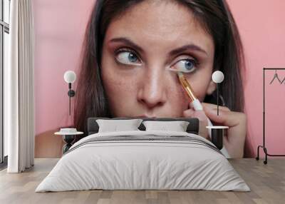 Close up of a young brunette woman with beautiful blue eyes applying eyeshadow with an eye brush Wall mural