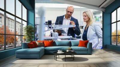 Confident businessman and businesswoman discussing while looking at machinery in factory Wall mural